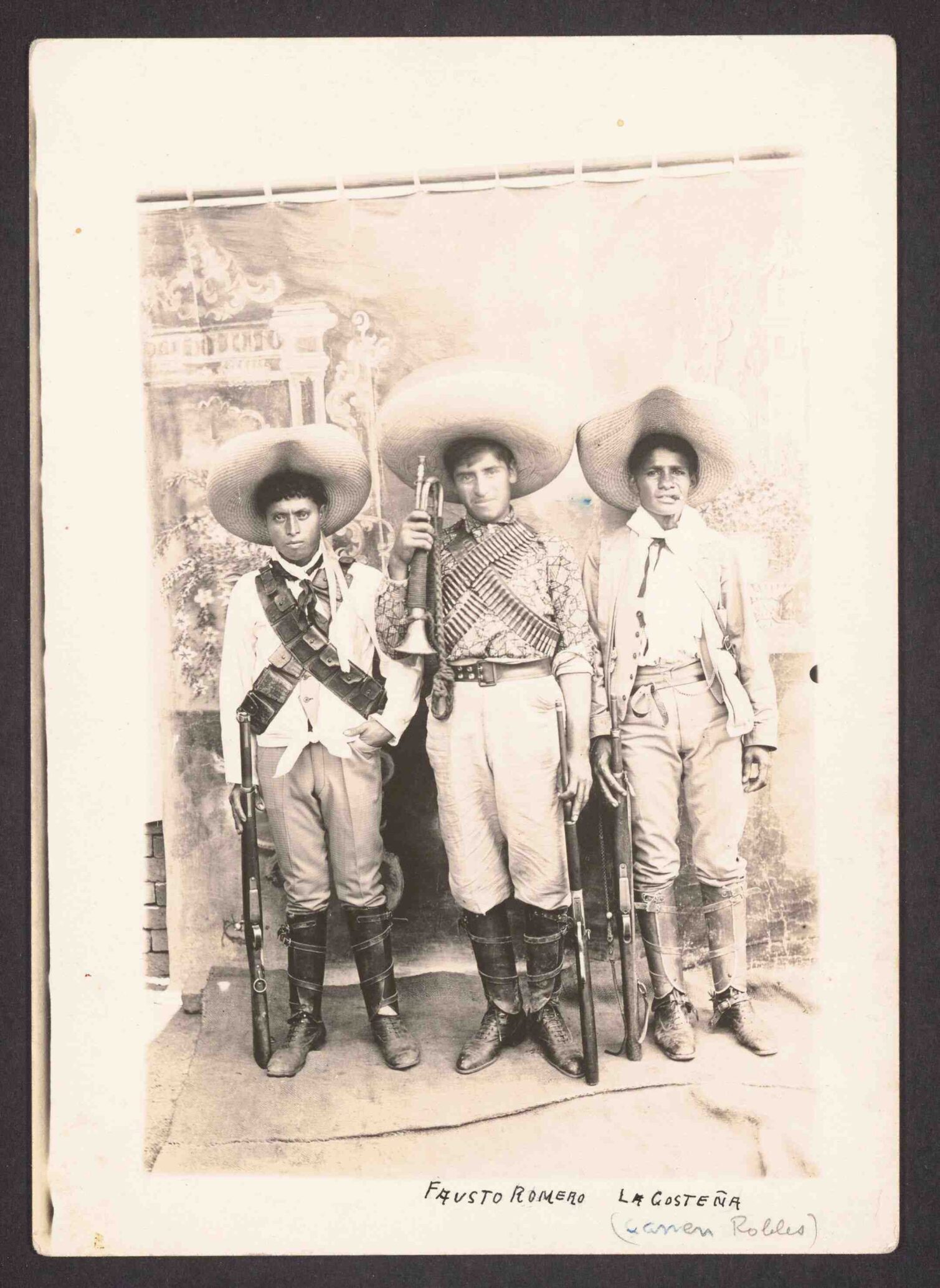 Three young men in traditional clothing and large hats, holding rifles.