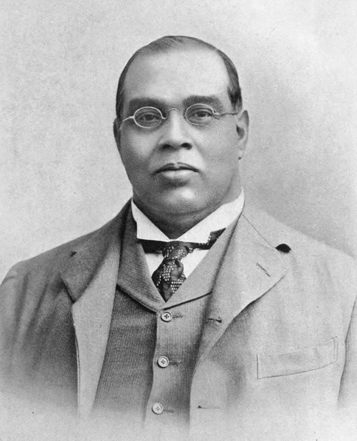 Portrait of a man in a suit and tie with glasses, smiling at the camera.