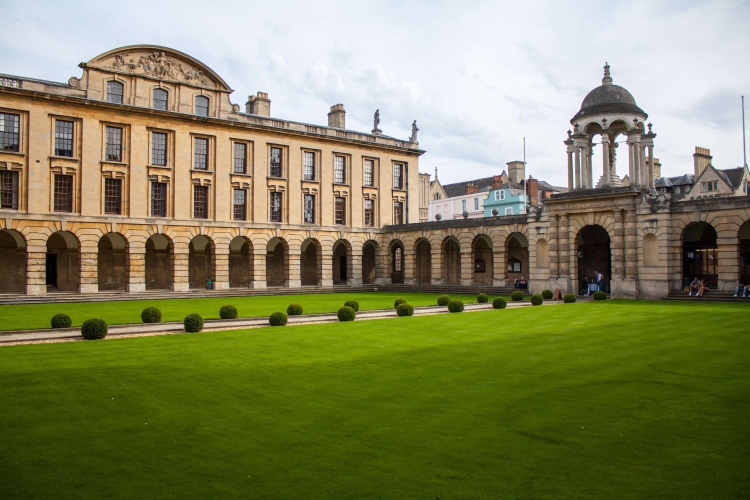A sunny courtyard with green grass, surrounded by stone archways and historic buildings.